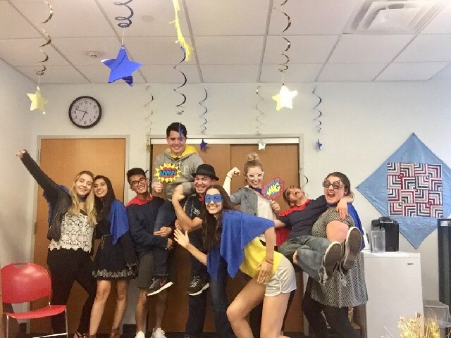 A group of students pose for a photo. They are wearing bright blue and yellow capes and masks.